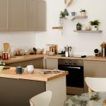 Part of modern spacious kitchen with row of cabinets hanging over counter with kitchenware and sink and electric stove with coffee pot