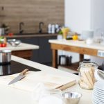 Modern workplace of cooking show: kitchen counter with cutting board, kitchen knife, open glass jar, stack of plates and bowl